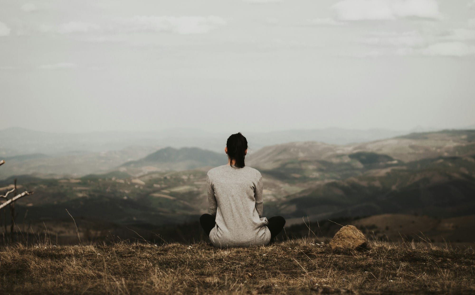 woman sitting on cliff overlooking mountains during daytime